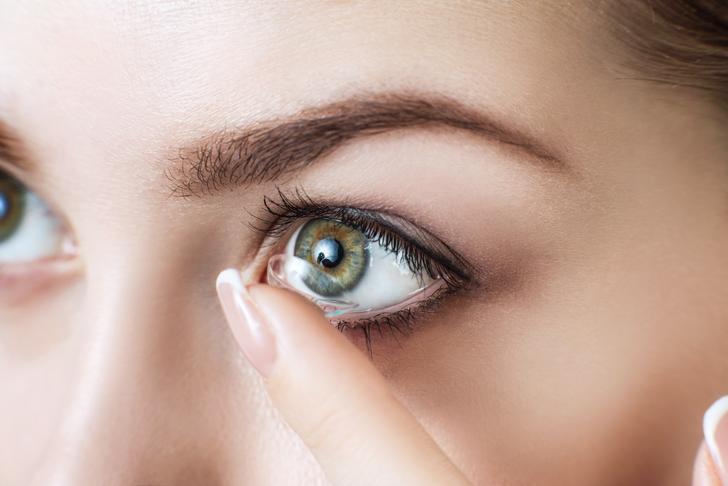 contact lens on a finger with contact lens packaging, case, and tweezers on a table