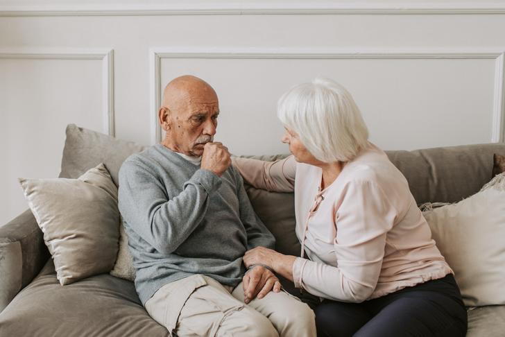 elderly woman sitting with elderly man coughing