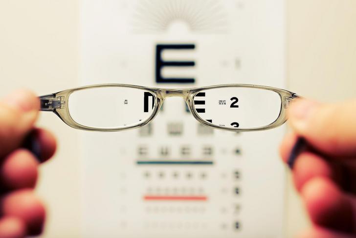 glasses being held up to a blurry eye chart