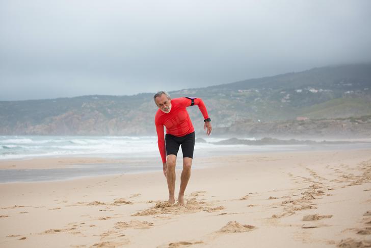 man holding foot while running on the beach