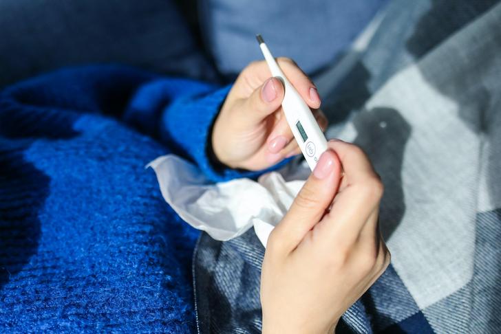 person holding thermometer and tissue in bed