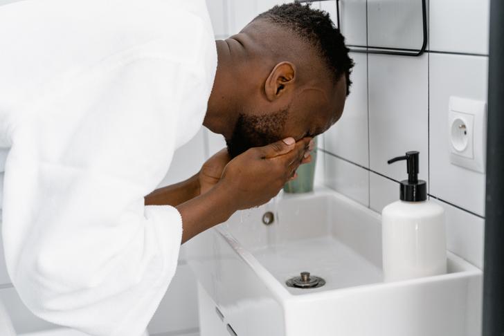 person over a sink rinsing eyes with water